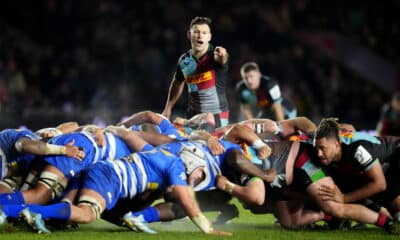 Intense rugby match scene with a scrum half poised to release the ball from the scrum, under the watchful eyes of competitors.