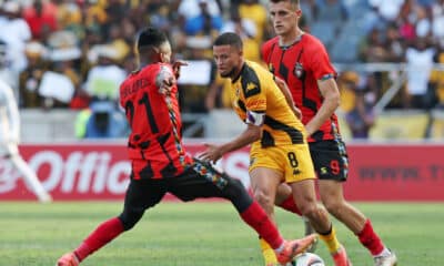 Dynamic action during a football match featuring Kaizer Chiefs and a rival team, with players intensely contesting the ball.